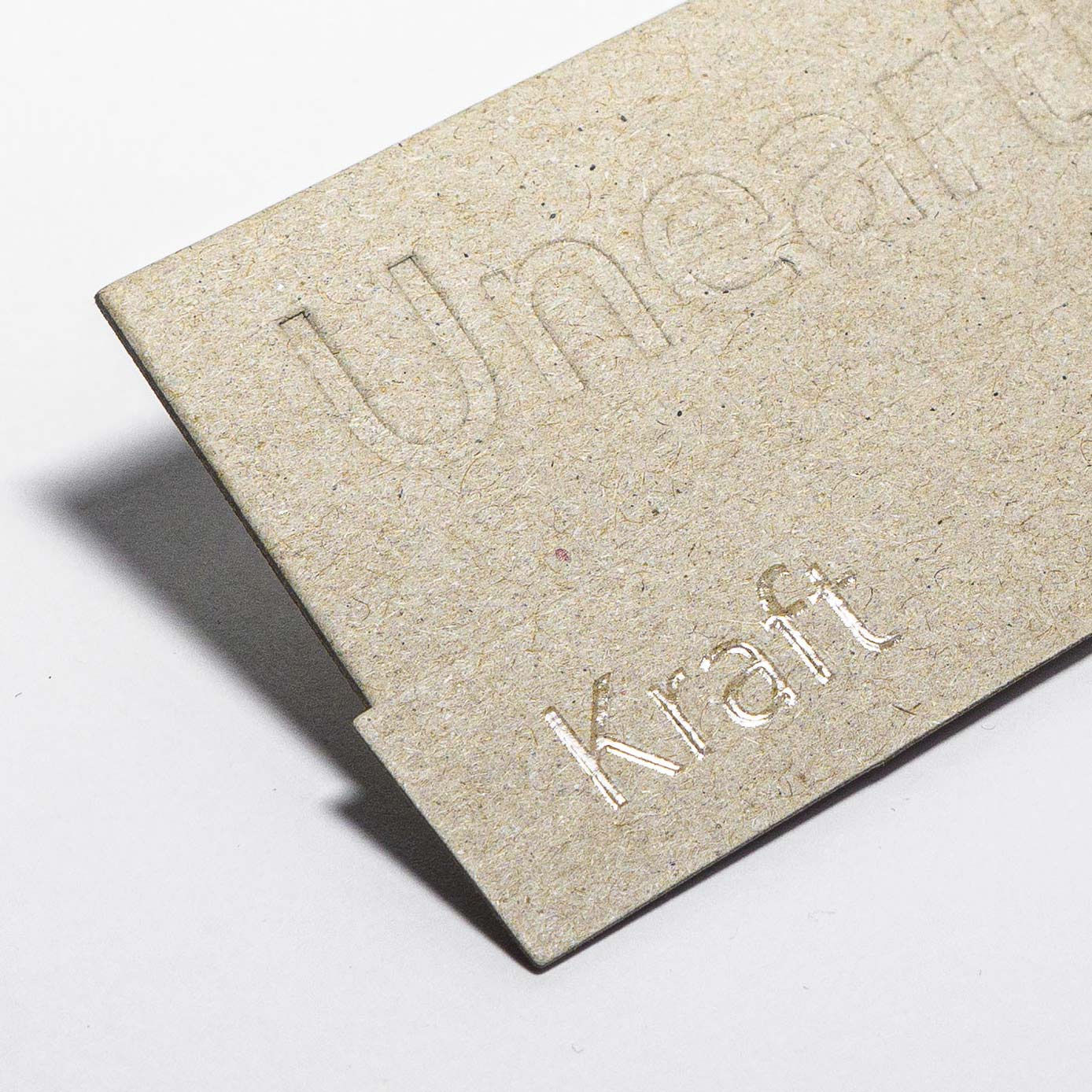 Grey board tag debossed with "Unearthed" and "Kraft"