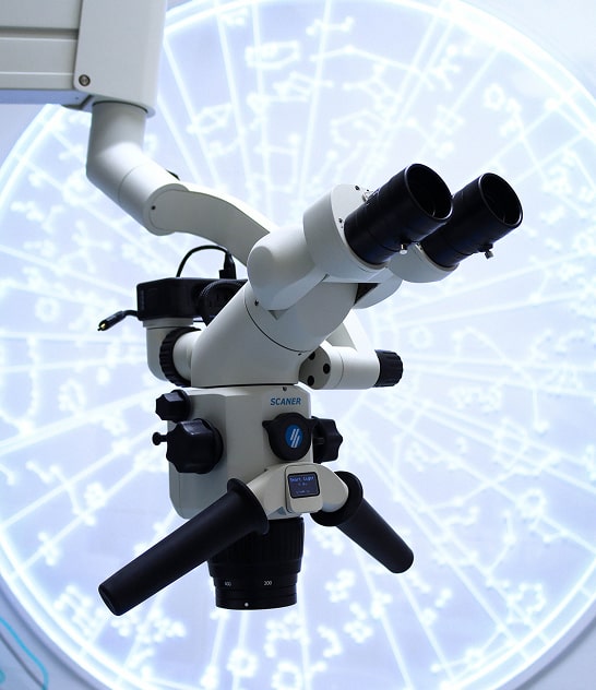 Chirurgien-dentiste ganté et masqué utilisant un microscope opératoire Carl Zeiss et tenant un instrument dentairé pour un traitement de précision