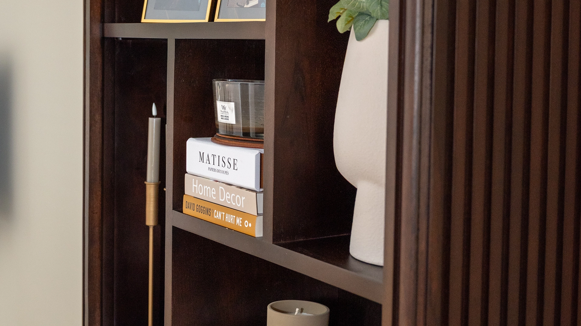 Close-up van een stijlvolle donkere houten kast met decoratieve boeken, kaarsen en design accessoires, interieurstyling door Nouk Interiors.
