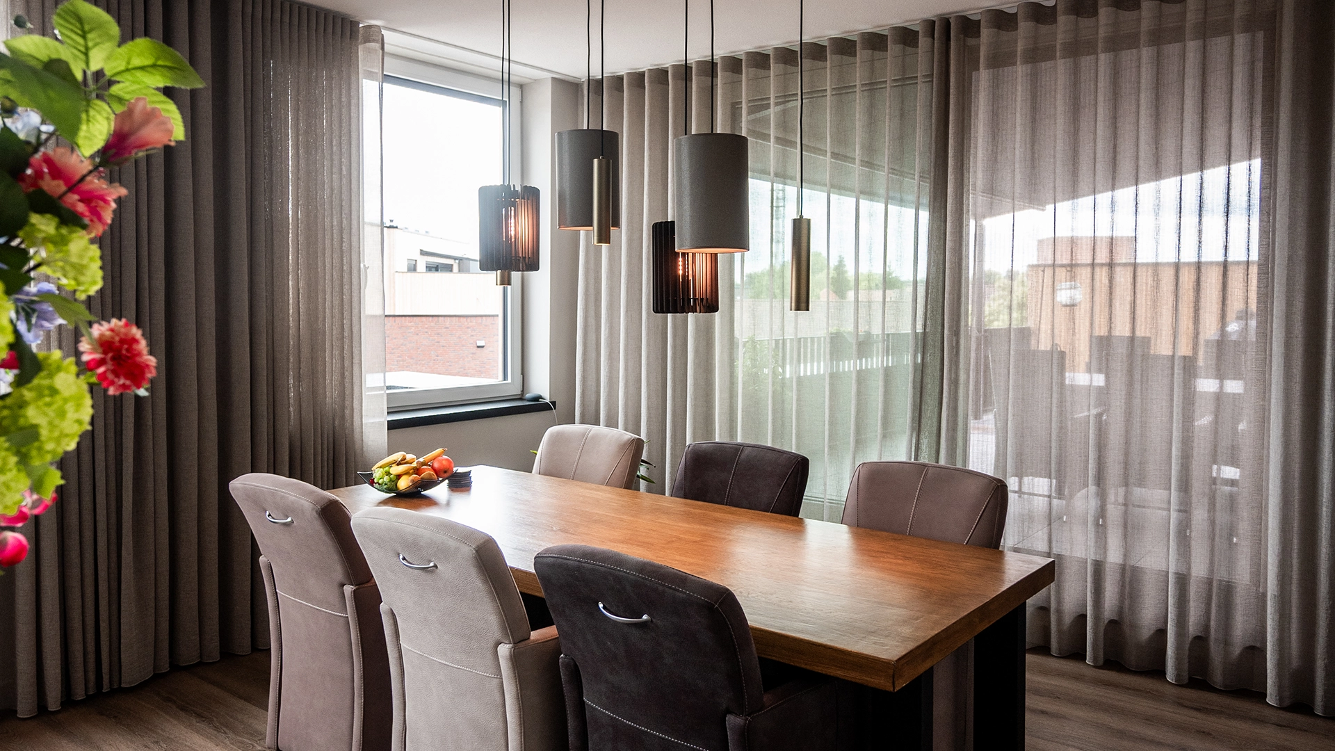Moderne eetkamer met houten eettafel, zes leren stoelen, sfeervolle hanglampen en grote raampartij met linnen gordijnen, ontworpen door Nouk Interiors.