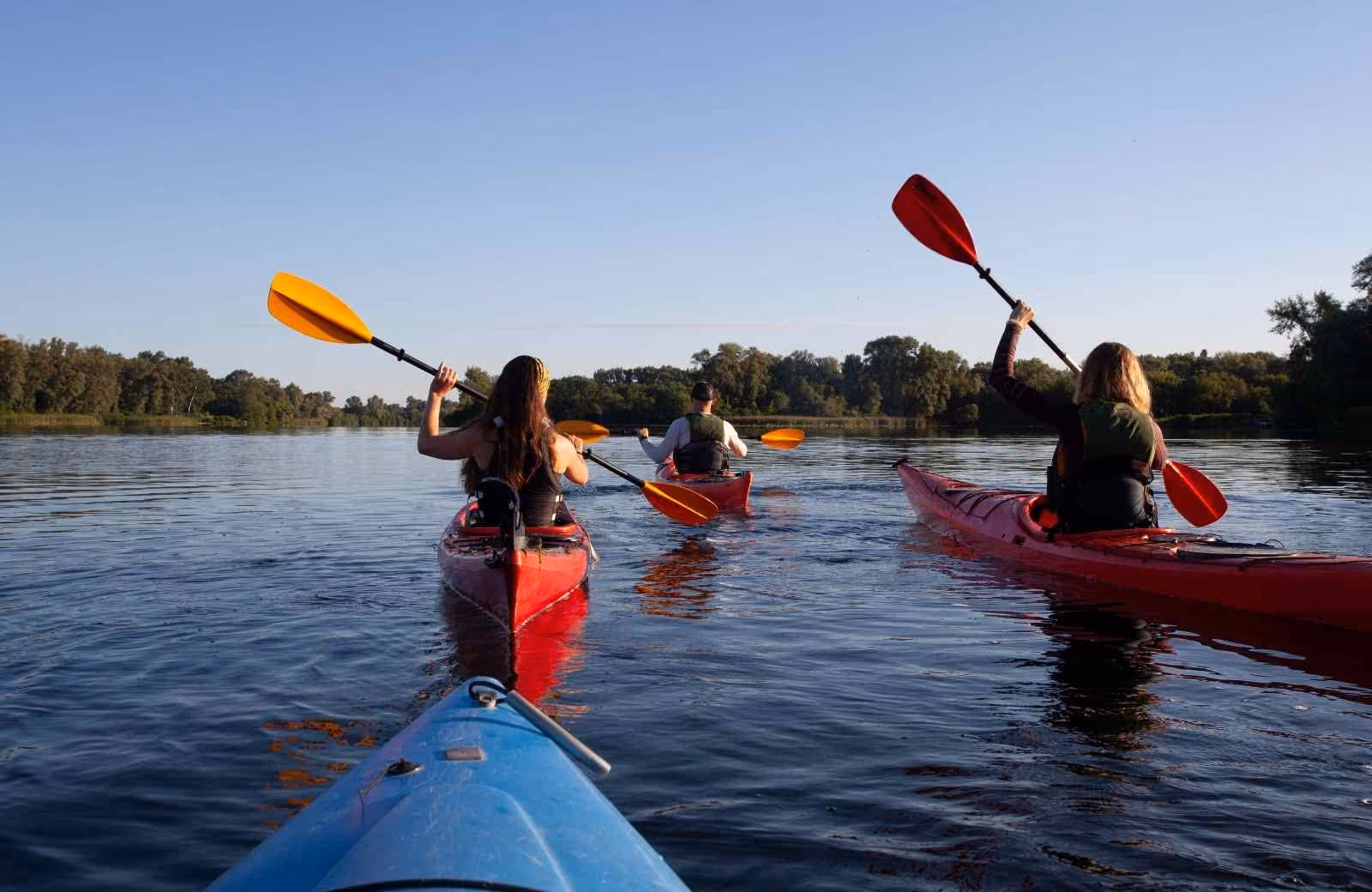 Groupe de trois personnes pagayant en kayak sur la Loire par temps calme, entouré de nature et d’arbres en fin de journée.