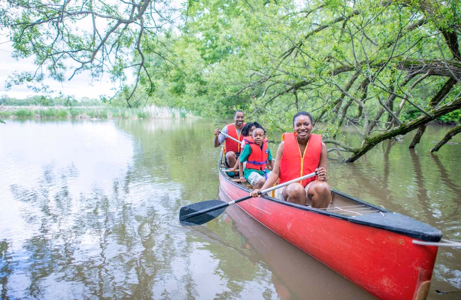 Famille pagayant ensemble dans un canoë rouge sur la Loire, entourée de végétation dense et d’eau calme.
