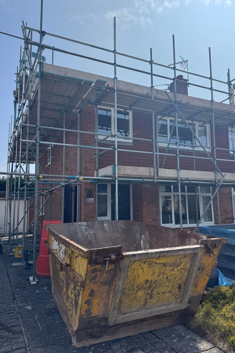 Construction site with scaffolding and yellow skip in front of brick building