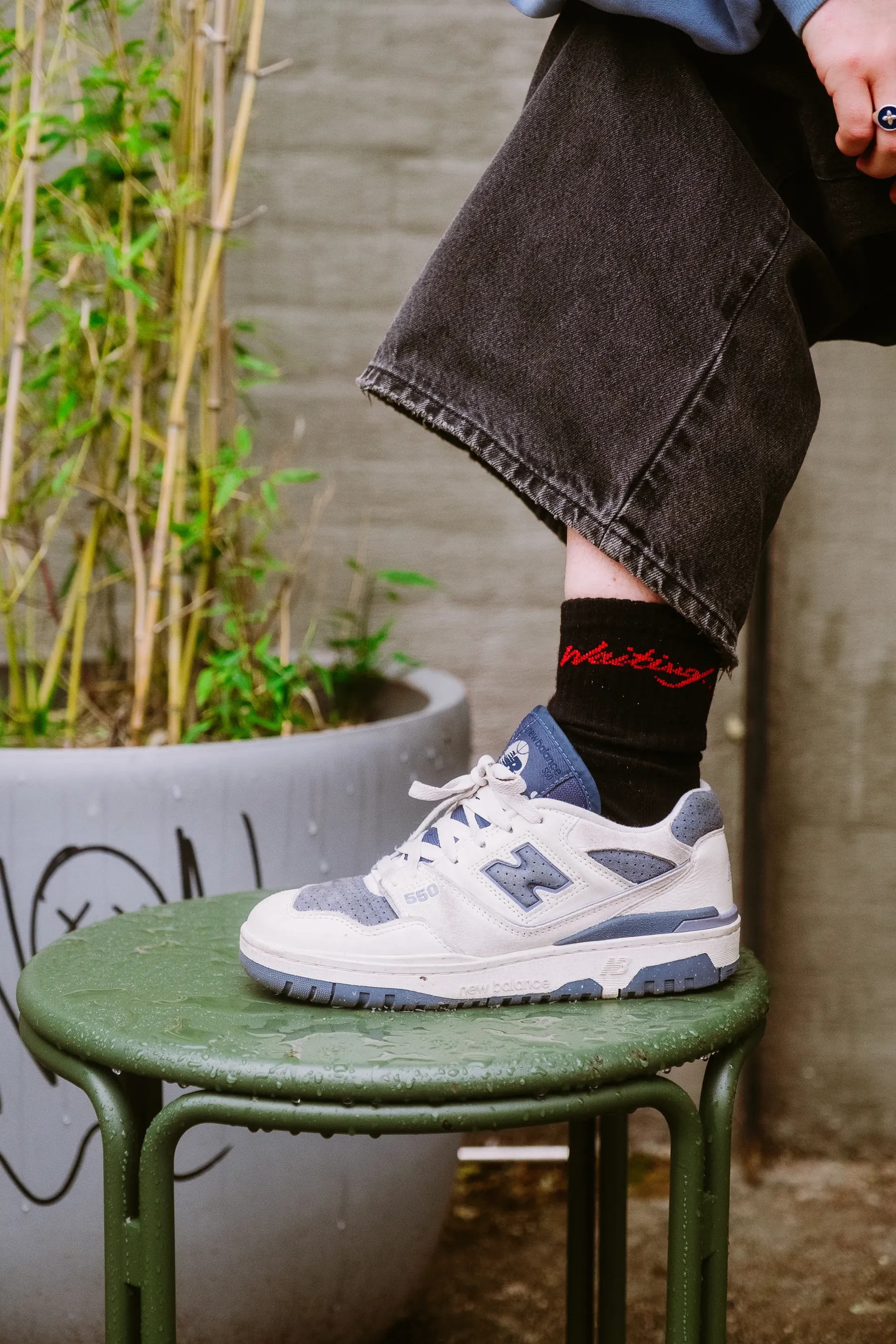 Wearing Waiting socks with white sneakers, one foot up on a green stool