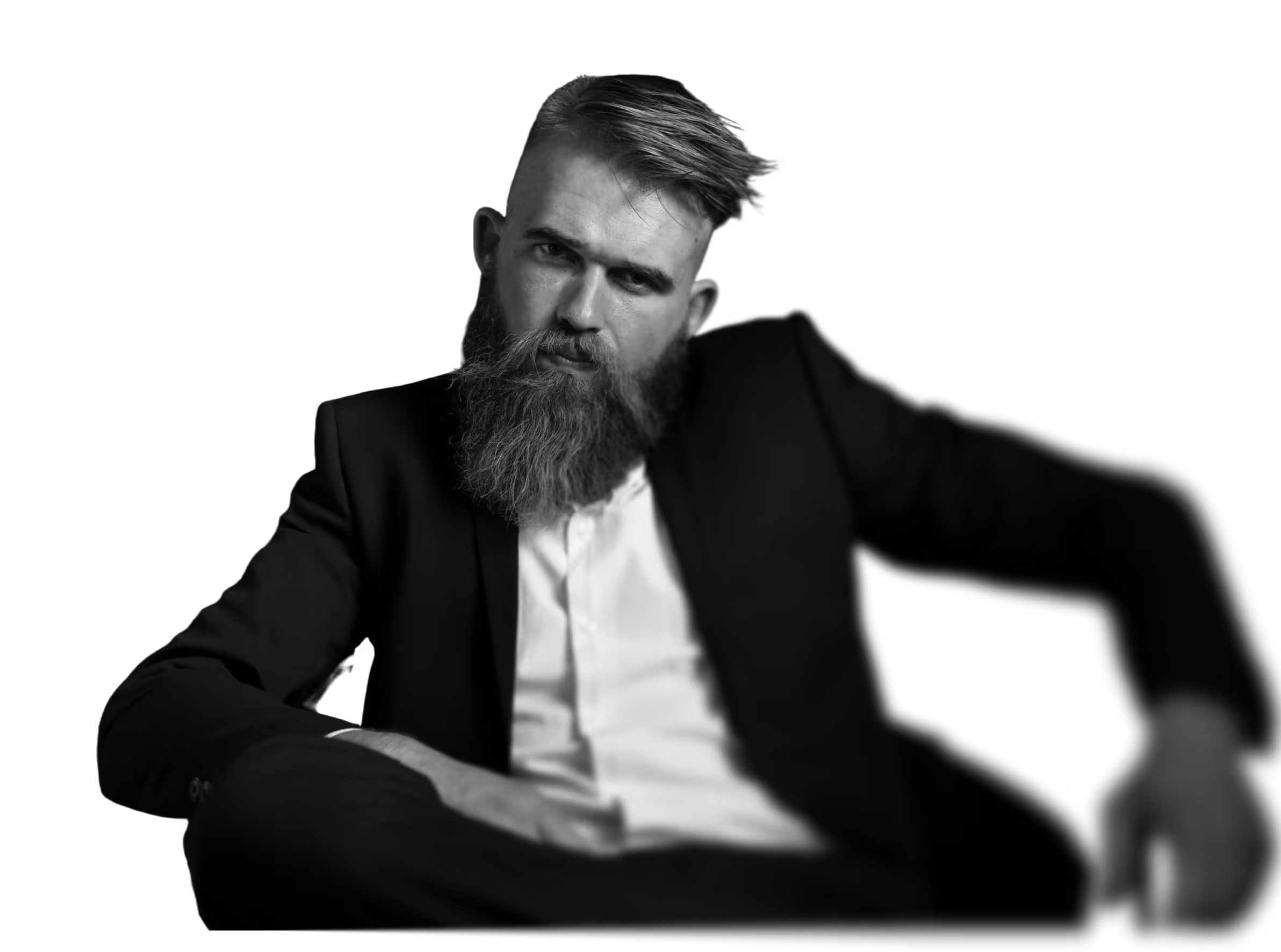 Black and white image of a young man with a long beard in a suit, sitting and looking straight into the camera