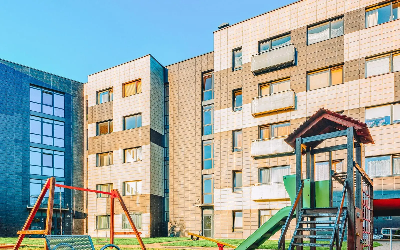A playground in front of a multi - story building.