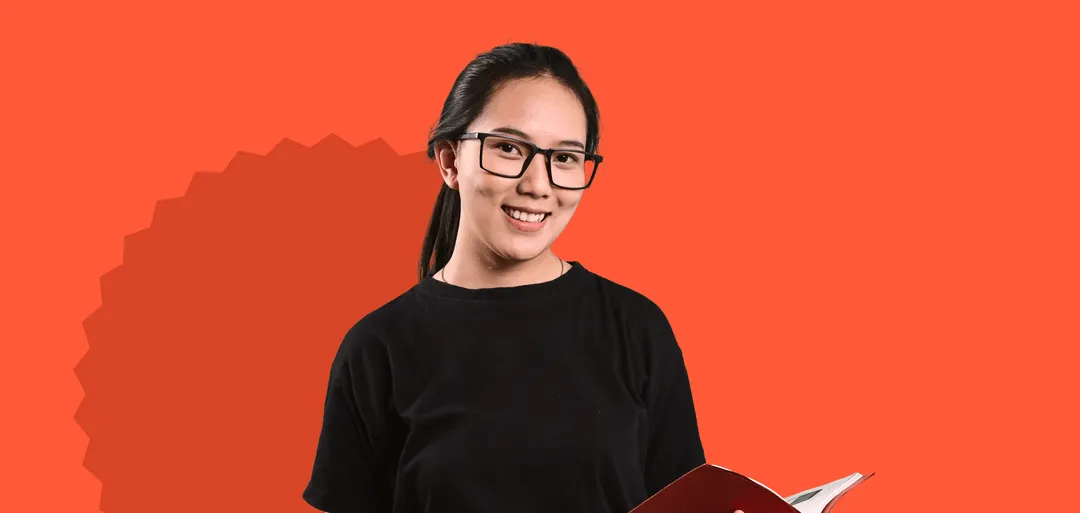 A woman with glasses holding a book and smiling.
