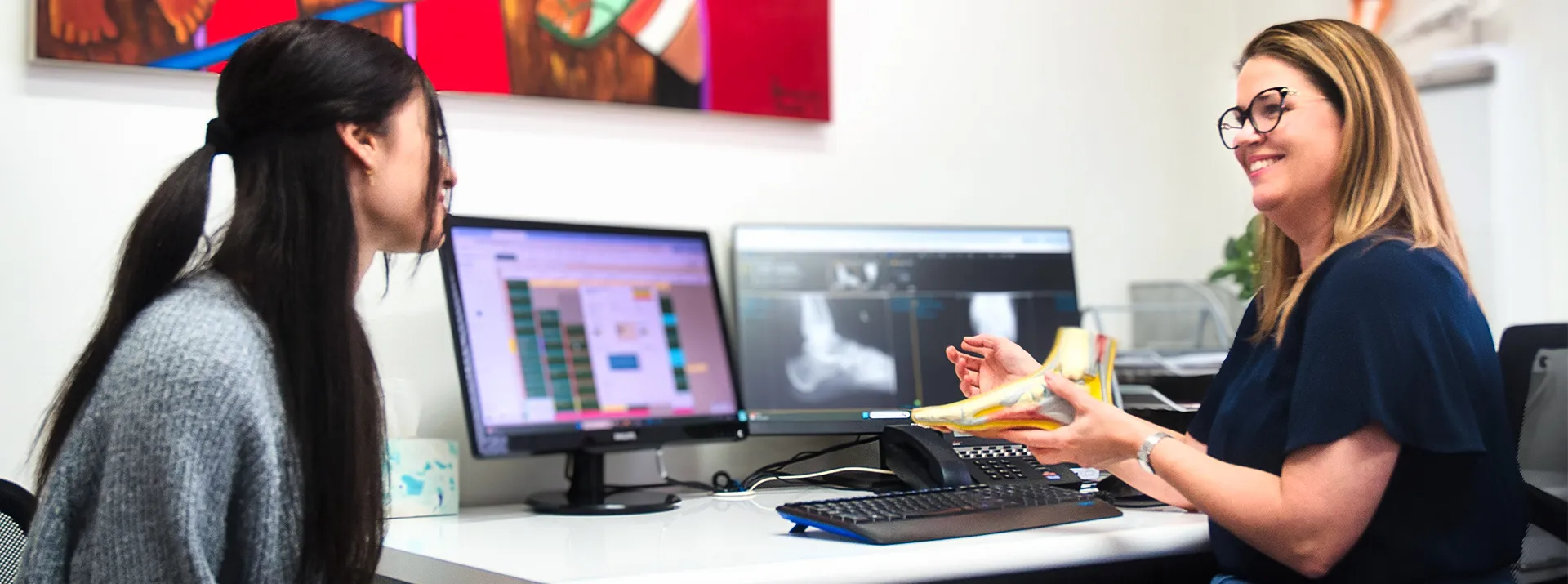 A podiatrist shows a patient a model of a foot during a consultation.