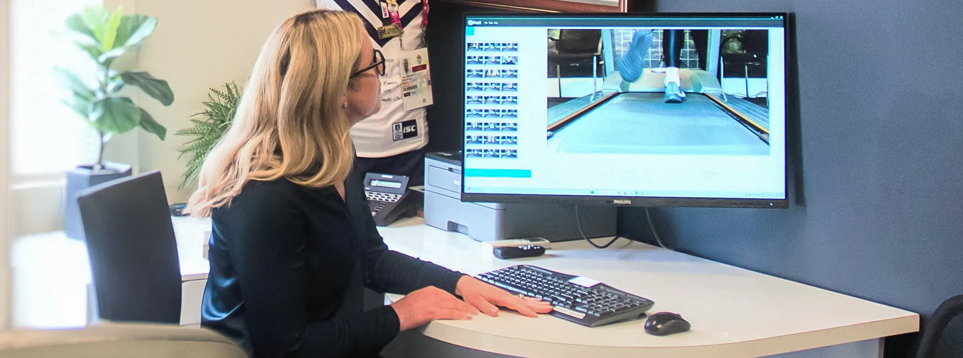 Woman views gait analysis footage of a person walking on a treadmill on a computer screen.