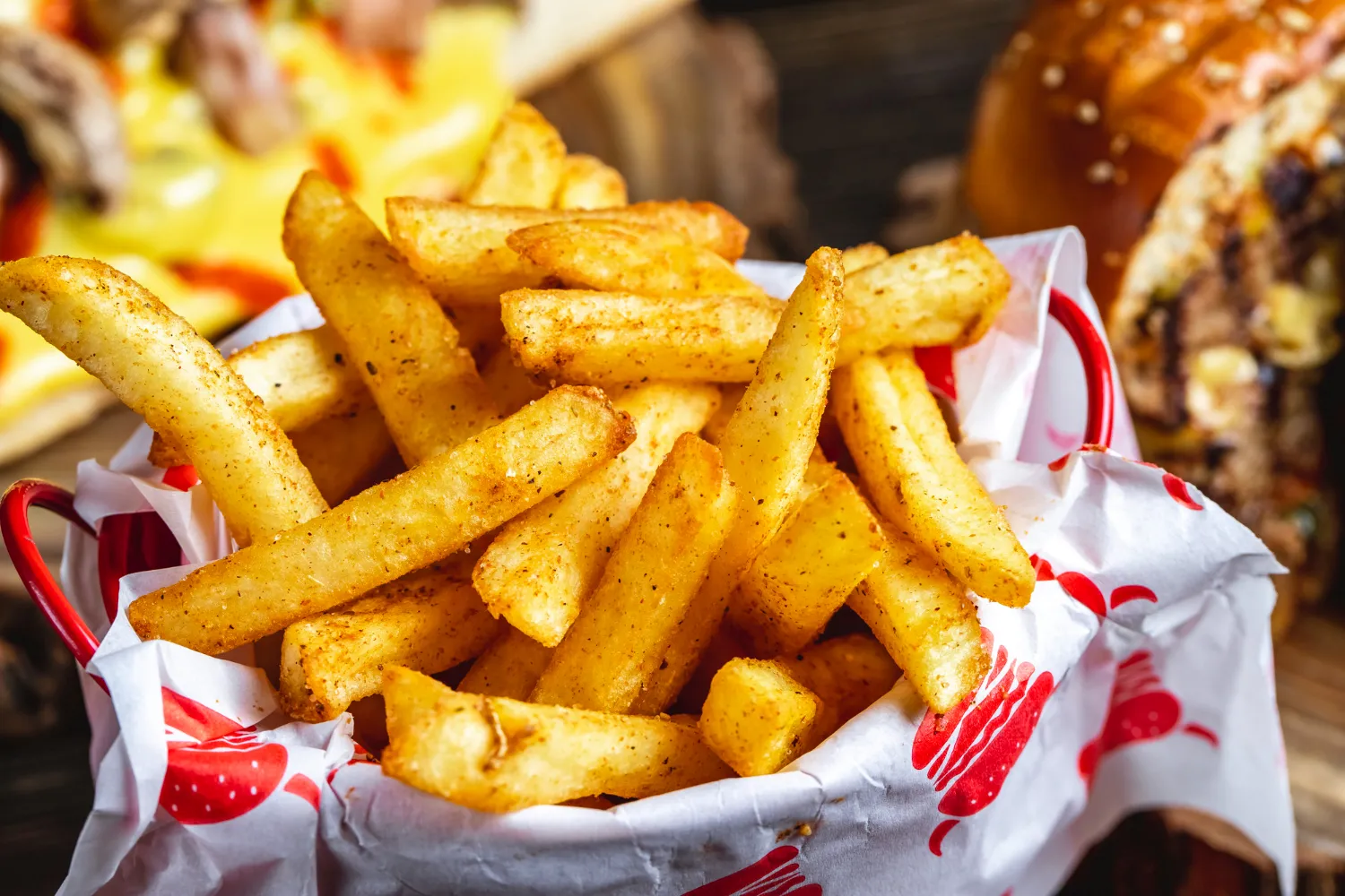 A basket filled with french fries next to a burger.