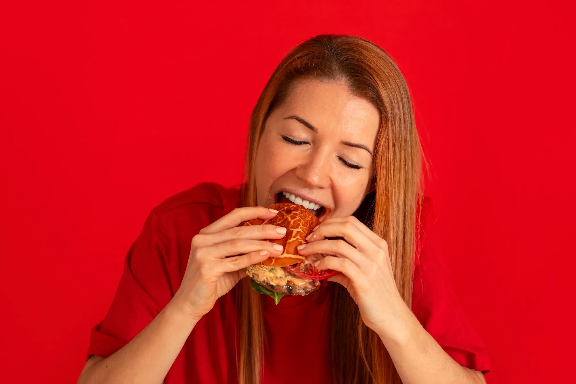 A woman in a red shirt is eating a sandwich.