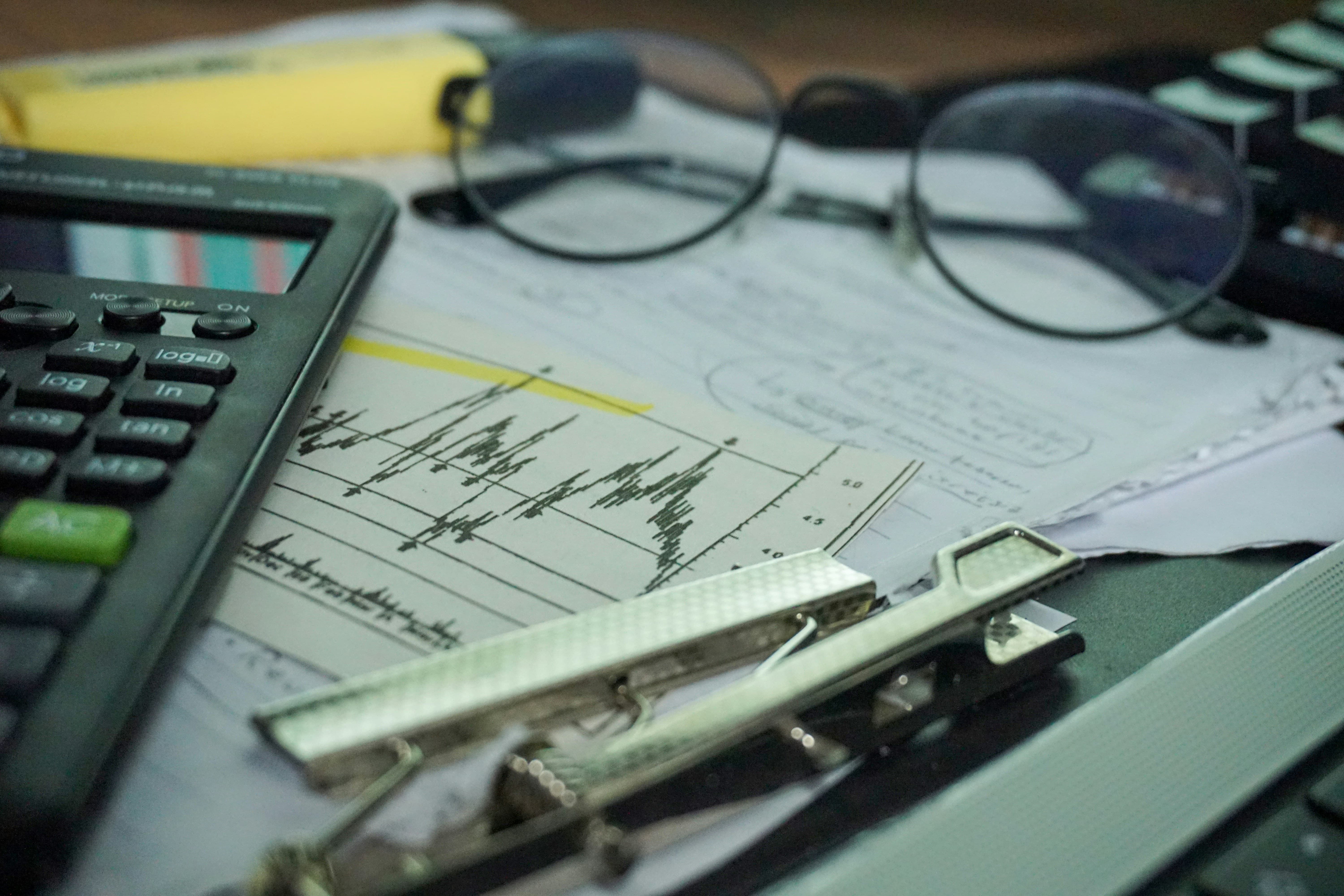 A desk with calculator, documents and a pair of glasses. 