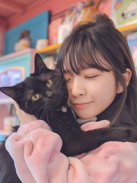 A girl in a pink coat holds a black cat, smiling gently as she stands outdoors