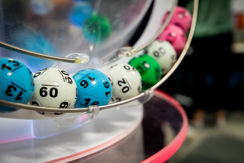 A close-up shot of a lottery machine with numbered balls in various colors, including blue, white, and green, as they spin in the machine.