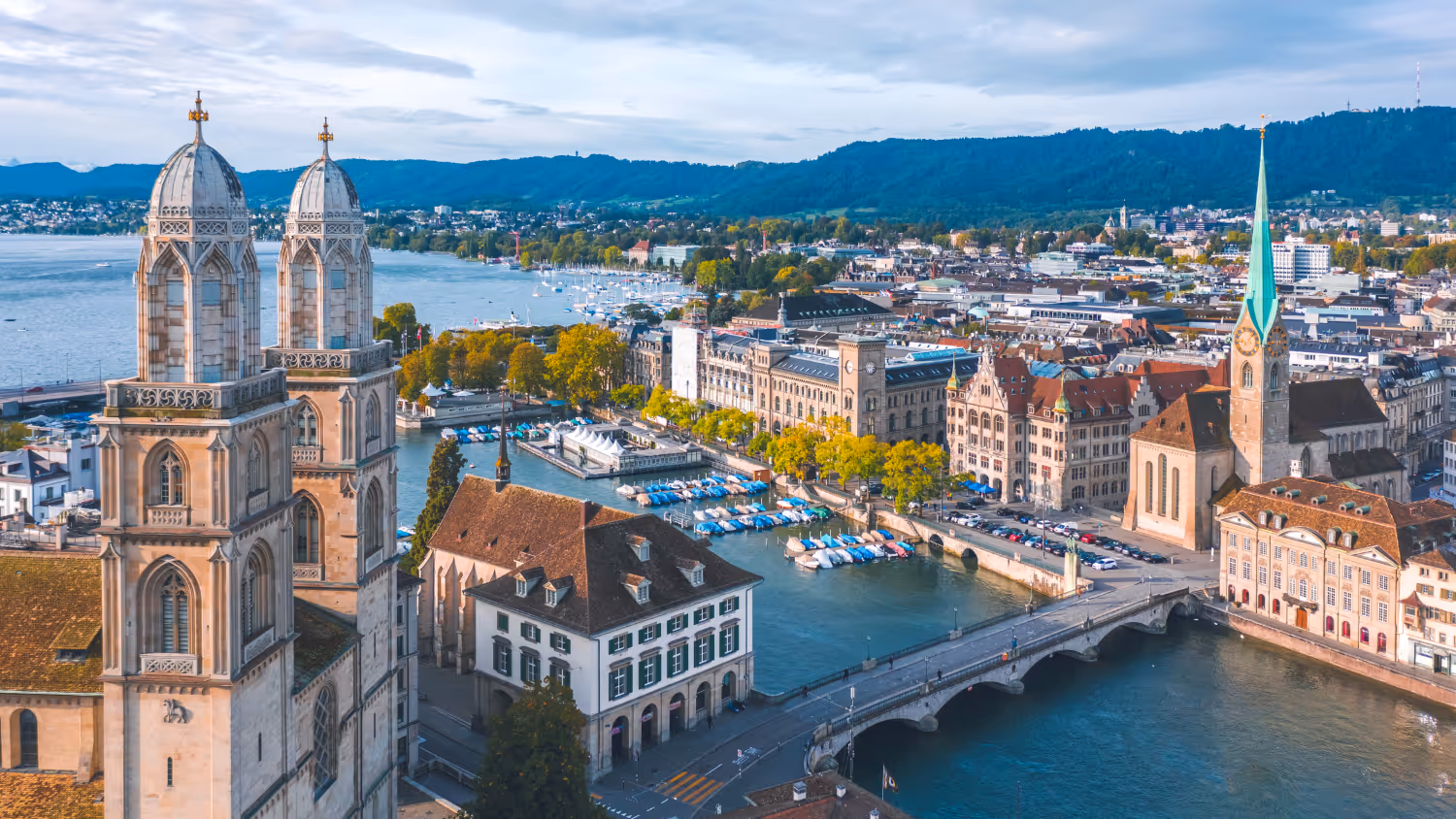 Aerial view of Zurich cityscape with the medieval St. Peter church clock tower and colorful riverside buildings along the Limmat River.