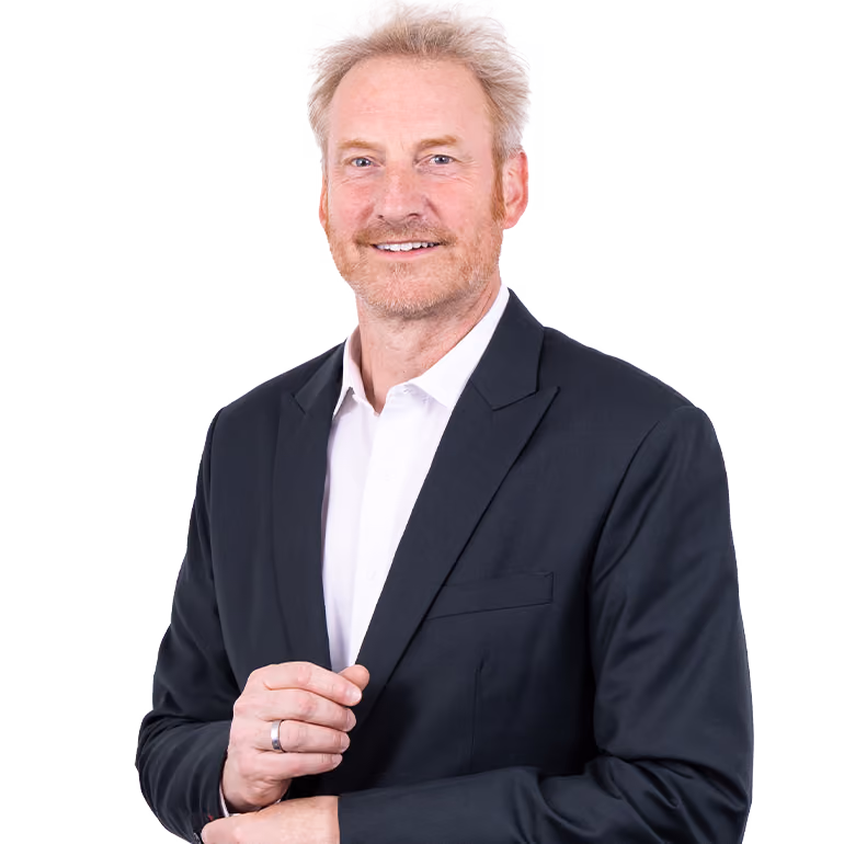 Geschäftsmann mit hellblonden Haaren und Bart, lächelt und trägt einen schwarzen Anzug mit weißem Hemd.