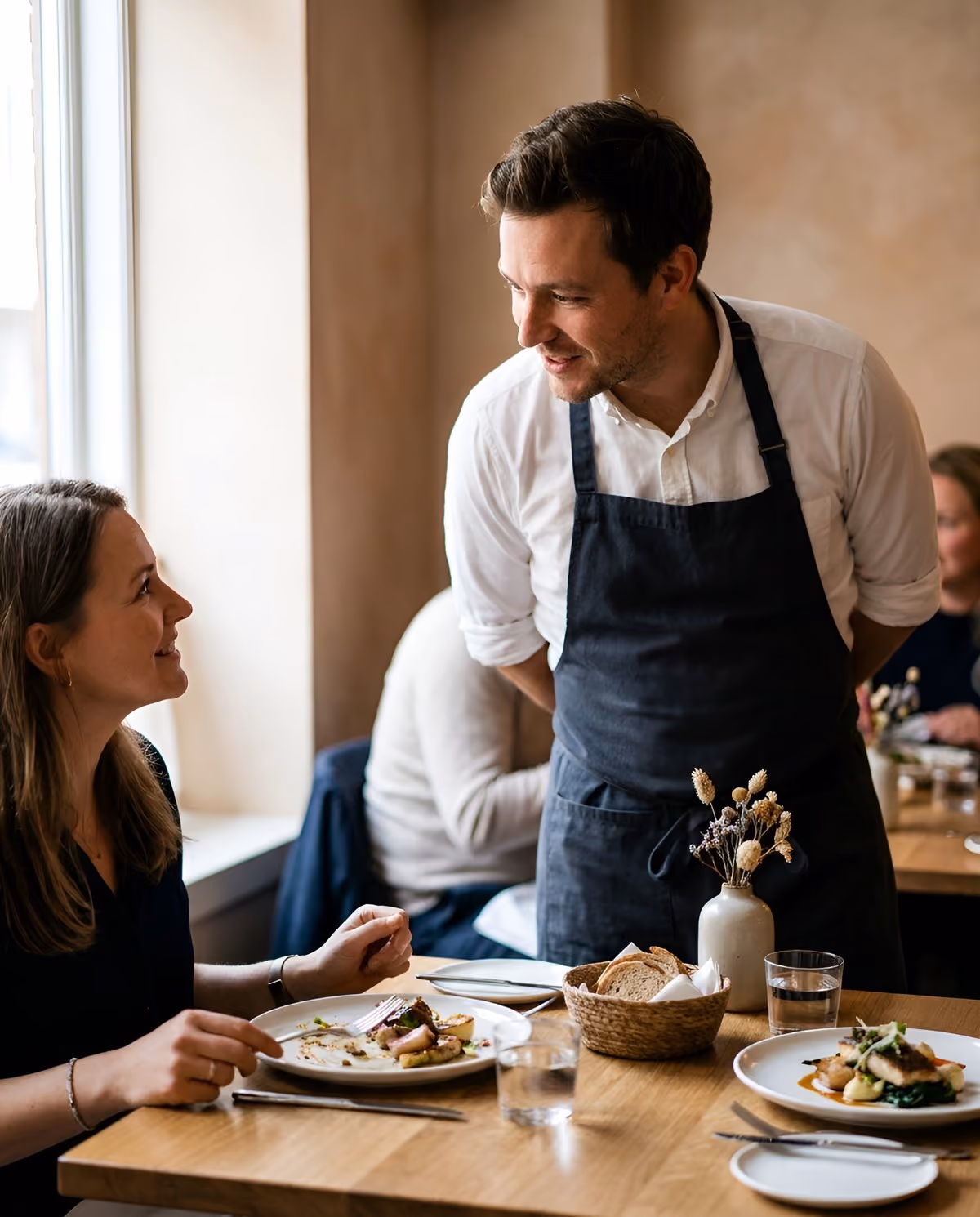 Waiter chatting with a guest at a restaurant table