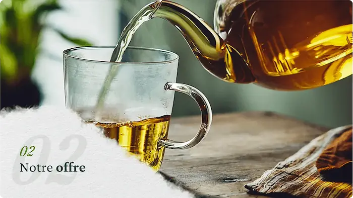 Théière versant du thé chaud dans une tasse en verre sur une table en bois.
