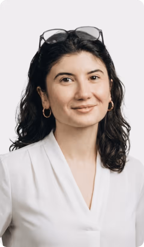 Femme avec cheveux bouclés, lunettes sur la tête, boucles d'oreilles, portant une blouse blanche.