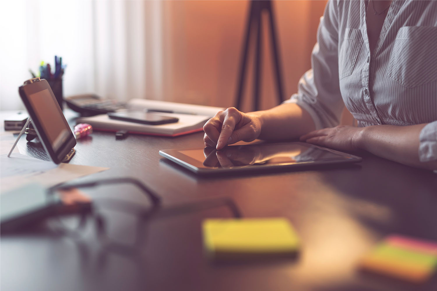 Someone sat at a desk with a tablet and a notebook writing copy.
