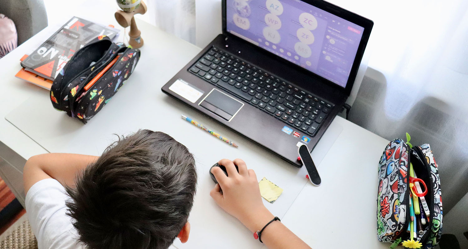 An ariel shot of a young schoolboy sat at his desk at home with his laptop open.