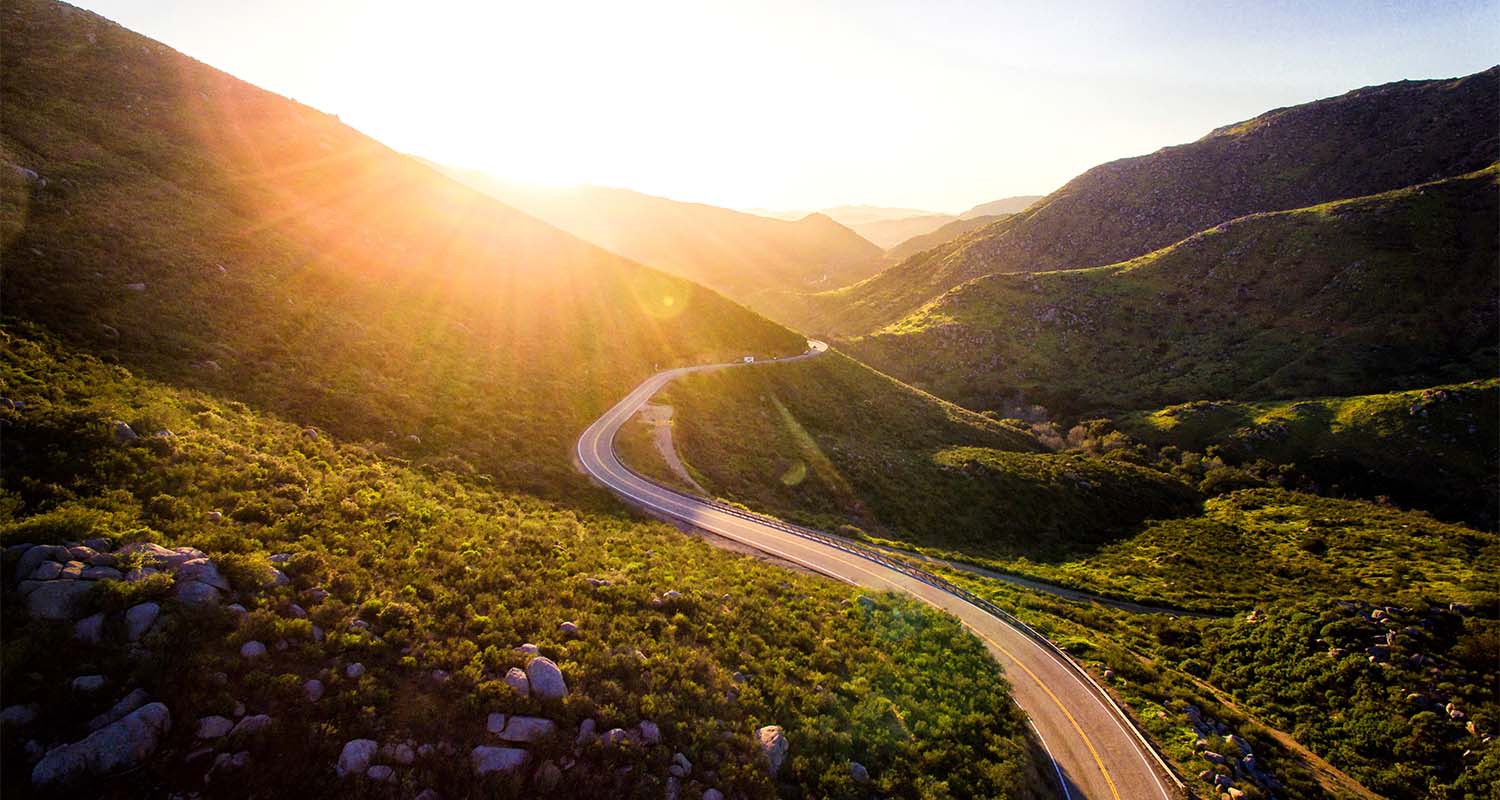 A beautiful landscape showing a winding road through a valley with the sun rising in the background
