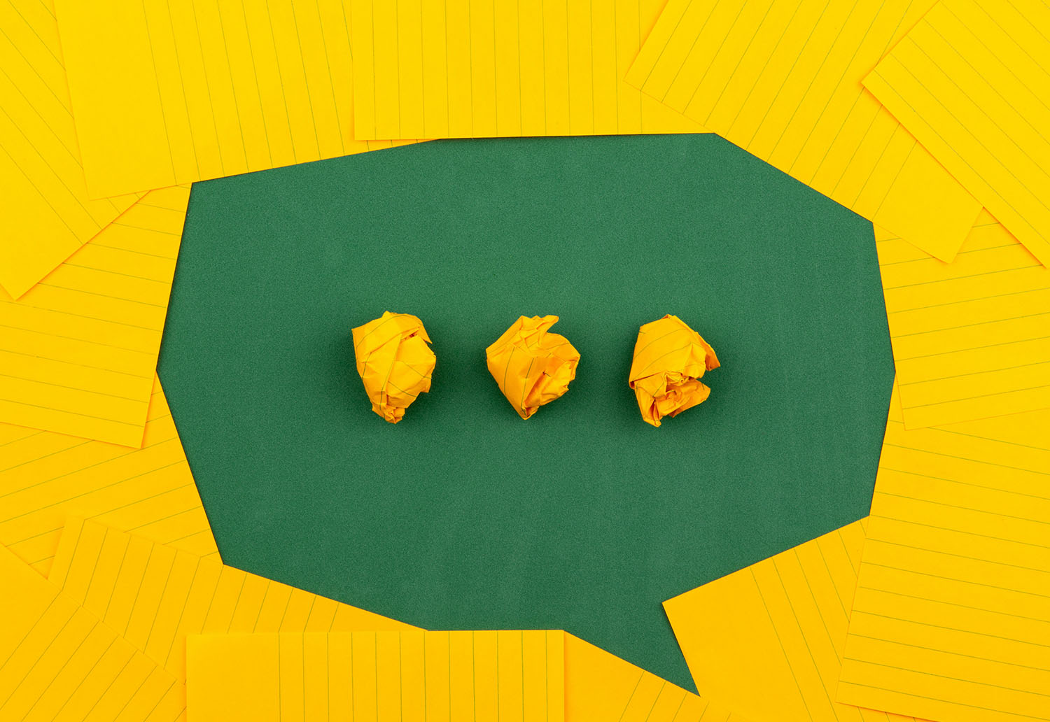 Yellow and green paper arranged in an origami style to create a speech mark, with three full stops inside.