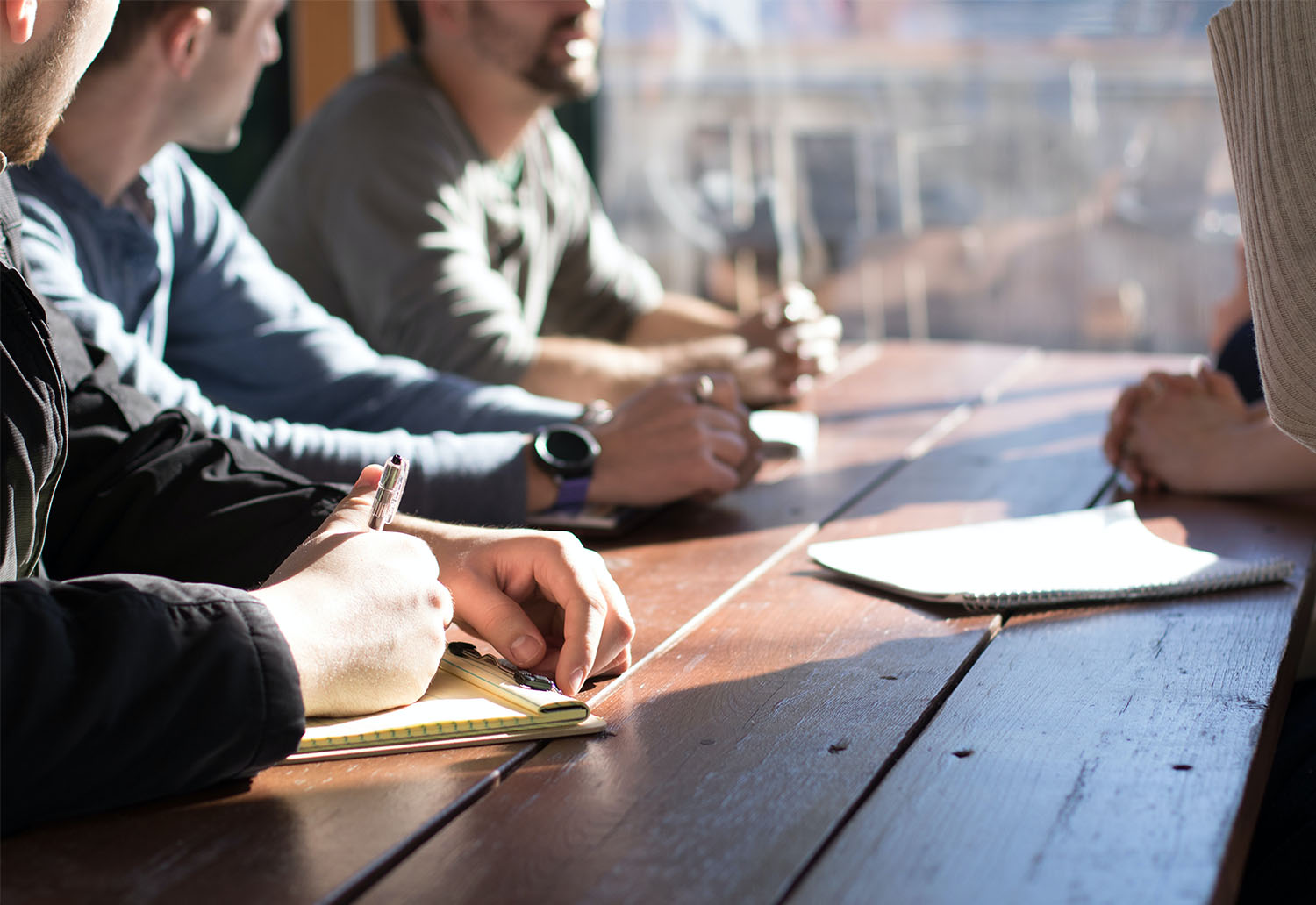 A group of people sat around a table with notebooks out, the sun is shining