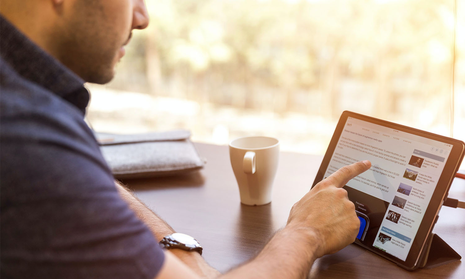 A man sat with a coffee scrolling on LinkedIn on his tablet