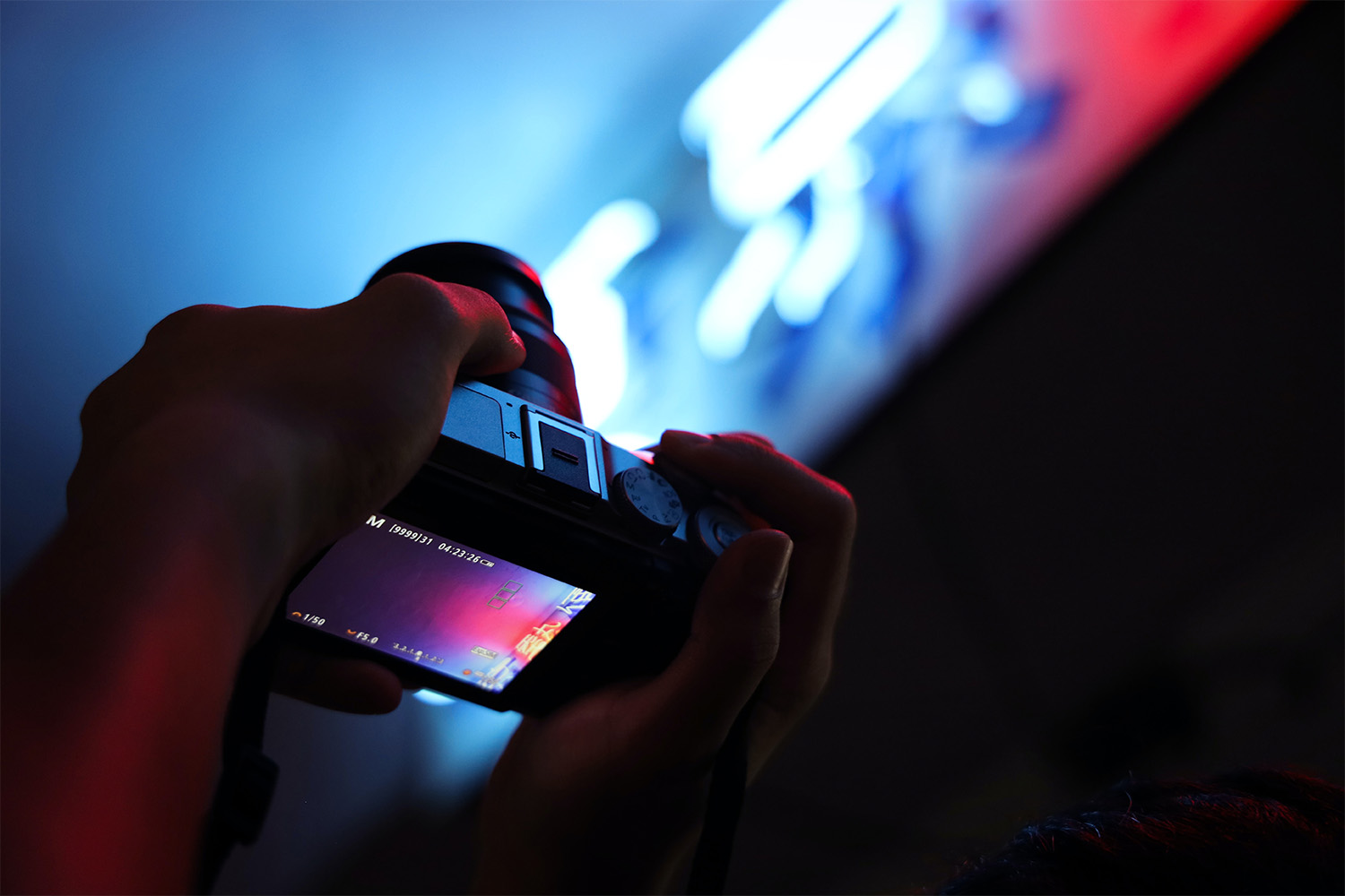 A dark image of hands holding a camera with bright lights visible in the background