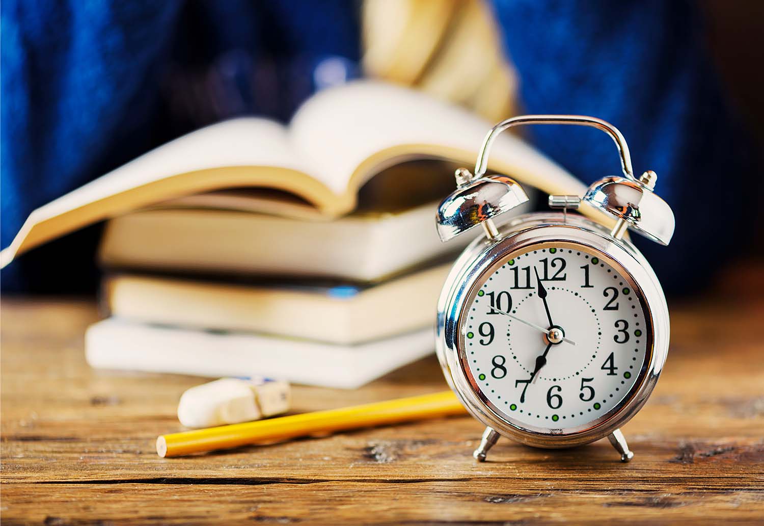 An old fashioned alarm clock next to a pile of homework