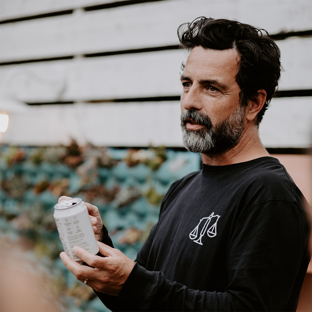 Something & Nothing Founder: A man with black hair and a beard holding a can of drink while talking to someone out of shot. 