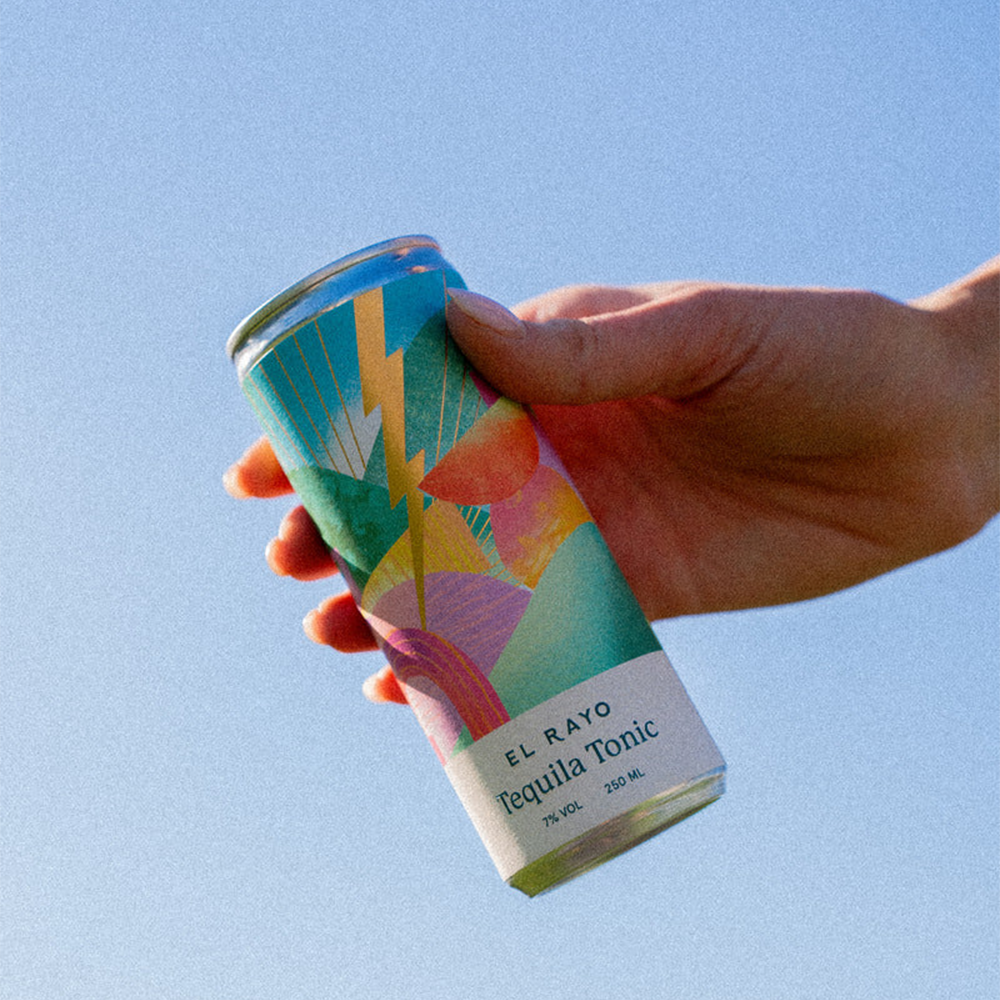 El Rayo Can being held by a hand in front of a sky background.