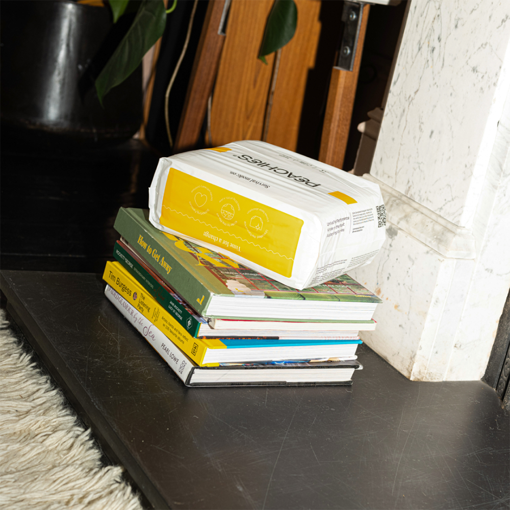 A package of nappies piled on top some books, in the corner of a room.