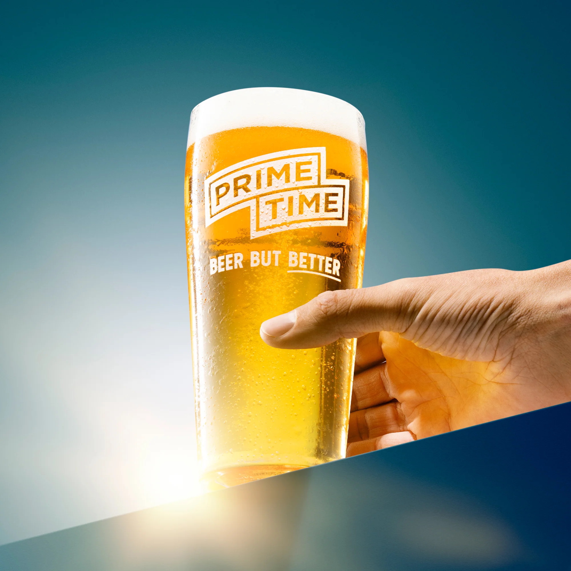 A hand holding a pint glass of beer. Glass has 'prime time' logo on it. 