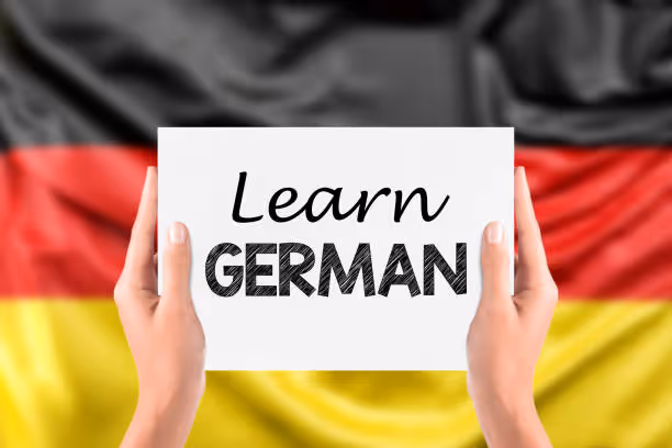Two hands holding a white card with the text 'Learn GERMAN' in front of a blurred German flag.