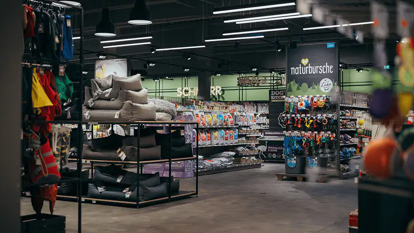 Interior of a pet store aisle displaying pet beds, toys, and various pet food products on shelves.