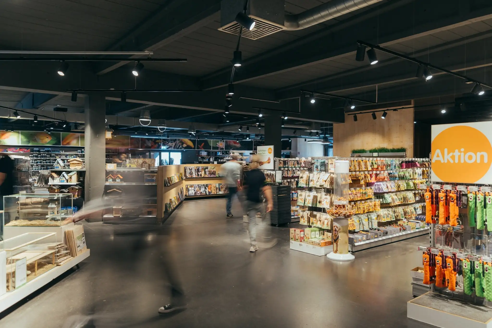 Interior of a pet store with shelves stocked with pet supplies and blurred figures walking in the aisle.