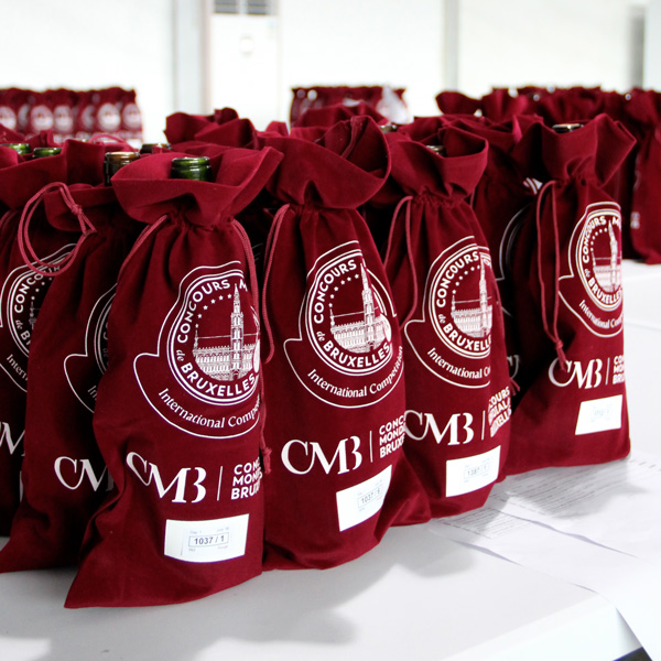 Wine bottles covered in red sleeves marked ‘Concours Mondial de Bruxelles,’ prepared for blind tasting at an international competition.