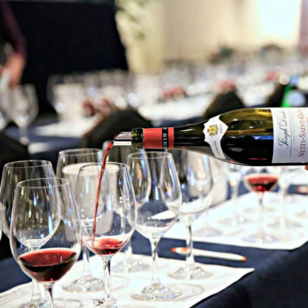Sommelier pouring red wine into tasting glasses during a wine masterclass session.