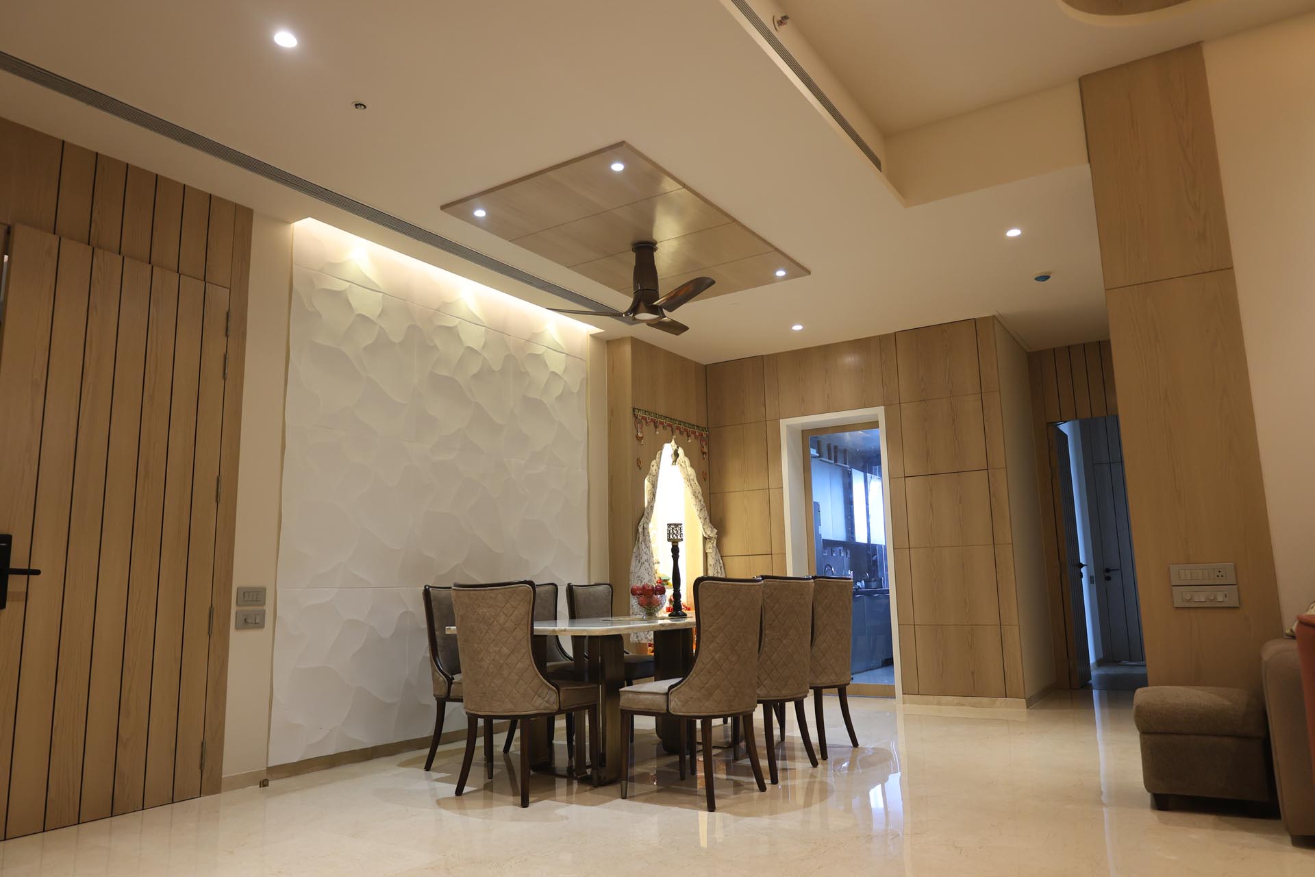 Spacious modern lounge area with rows of tan upholstered armchairs, wooden flooring, glass partitions, and large windows letting in natural light, accented by potted plants.