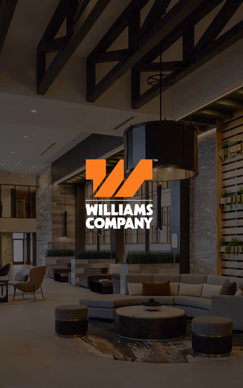 Modern lobby seating area with a large circular sofa, round tables, and stools under exposed ceiling beams.