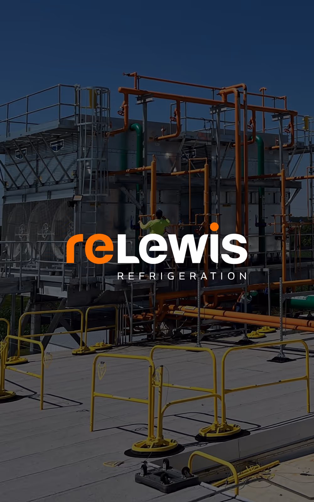 Industrial refrigeration equipment with orange pipes and metal platforms under a clear blue sky and a worker in a green shirt.