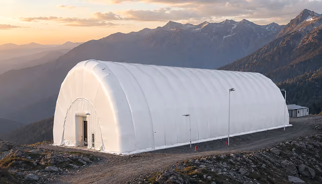 Large white fabric structure on rocky terrain with mountains and sunset in the background.