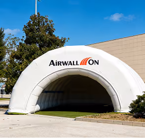 White inflatable Airwallon shelter set on pavement under a clear blue sky with trees and a building nearby.