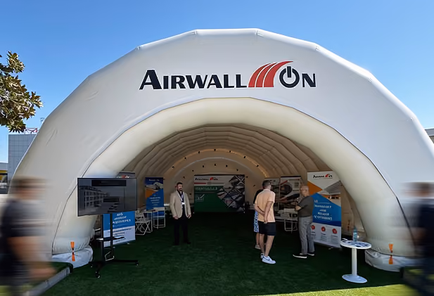 White inflatable Airwallon tent with people inside and display boards under a clear blue sky.