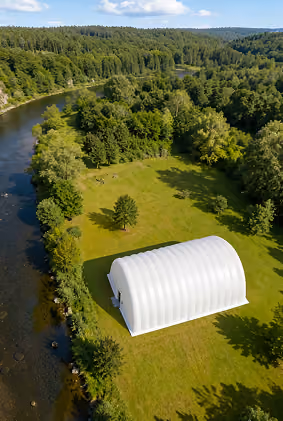 White inflatable building on green lawn near river surrounded by dense trees and forested hills.