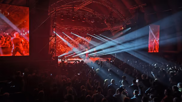 Crowd watching a live concert with bright stage lights and large screens in a dark venue.
