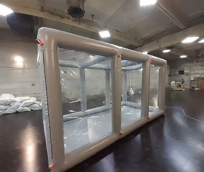 Large transparent inflatable isolation chamber with a gray frame in an indoor industrial space.
