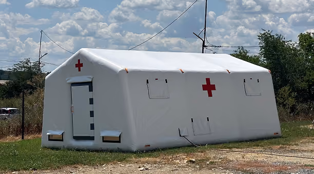 Large white inflatable medical tent with red crosses on its side and front, set outdoors on grass.